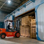 Man operating a forklift indoors loading wooden pallets in a warehouse.